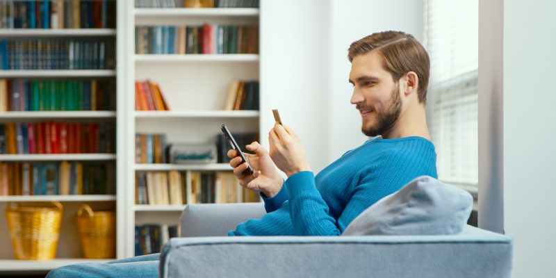 young-man-looks-at-bank-card-in-hand-and-enters-digits-to-smartphone.jpg